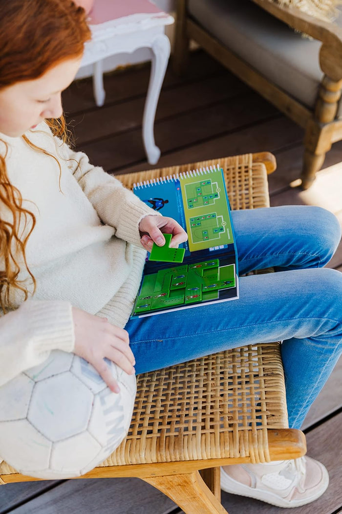 Portable soccer logic puzzle game with green pieces in a spiral-bound book, shown being played by a young girl.