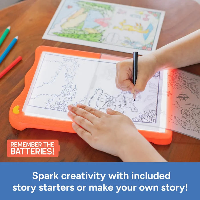 Child tracing a comic on an orange light-up pad with pencils and story starters on a wooden table.