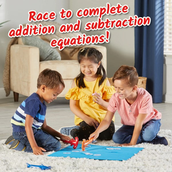 Three children use colorful shark hammers to pick up numbered tiles on a blue play mat.