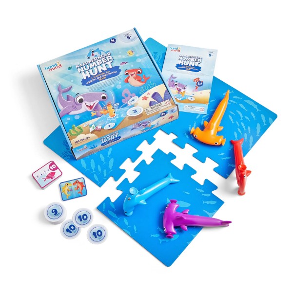 Math game with four colorful shark strikers, blue interlocking mats, number tokens, and cards next to the game box.