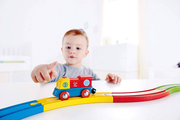 Toddler playing with a yellow and red toy train engine on a colorful wooden track.