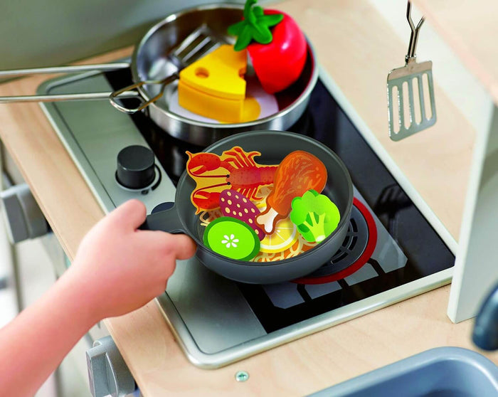 Child holding a toy frying pan with colorful play food over a stove with realistic glowing red burners.