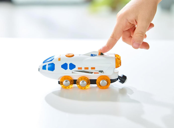 White space shuttle toy with blue windows and translucent orange wheels, with a child's finger pressing a top button.
