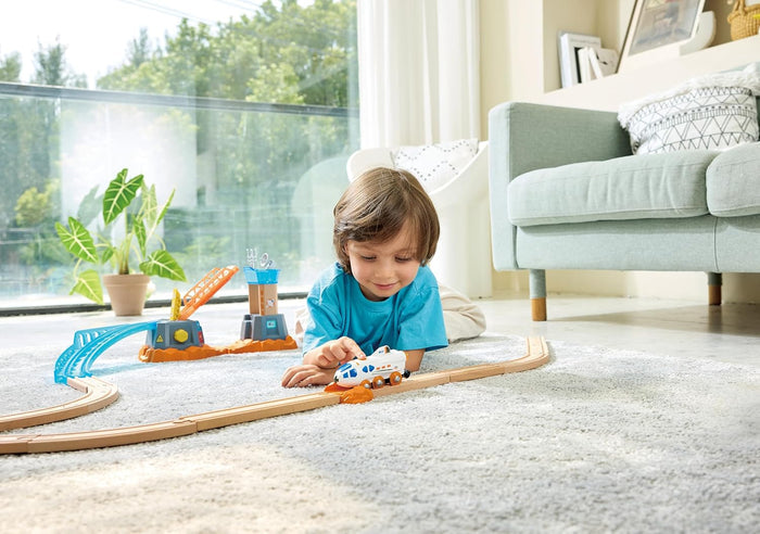 Child plays with white space shuttle train on wooden tracks with a blue bridge and orange crane station.