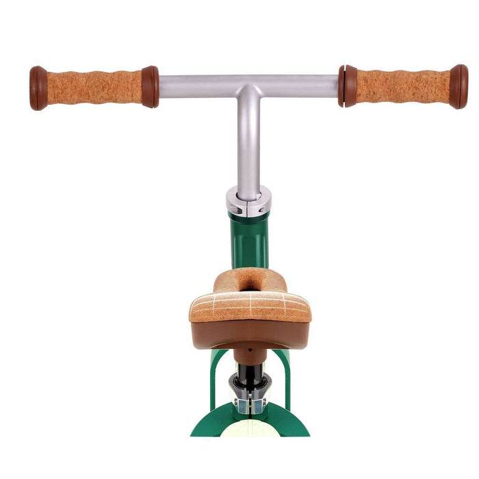 Front view of a green and silver balance bike with cork-textured grips and a tan patterned saddle.