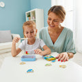 Woman and child play with a wooden magnetic fishing game featuring colorful fish and a blue metal storage tin.