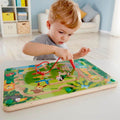 Toddler using a red magnetic wand on a wooden jungle-themed maze board with colorful wild animal illustrations.