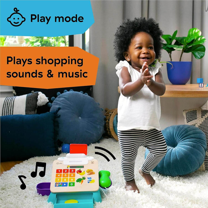 Wooden toy cash register with colorful buttons next to a happy toddler clapping on a plush white rug.