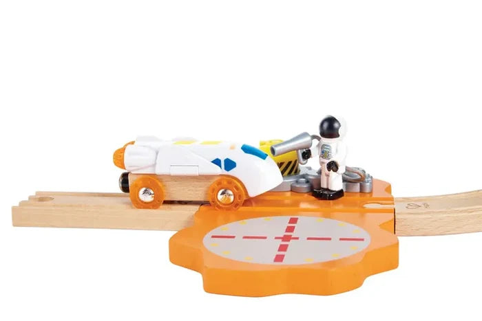 White wooden space shuttle on tracks with an astronaut figure and an orange gear-shaped landing pad.