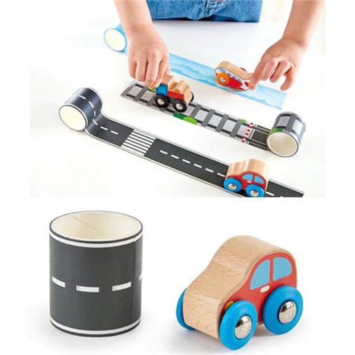 Child playing with toy cars on road and track tape. Close-up of wooden red car and black road tape roll.