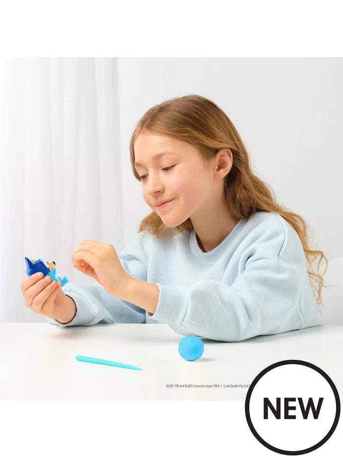 A girl sculpting a blue clay character at a white table with a blue clay ball and a turquoise sculpting tool.