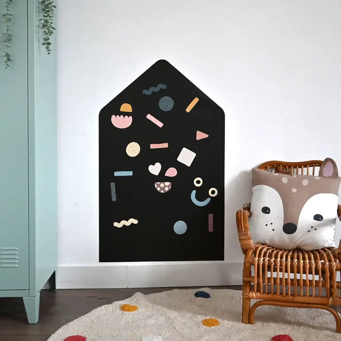 House-shaped black magnetic board on a white wall with colorful magnetic shapes in a child's room.