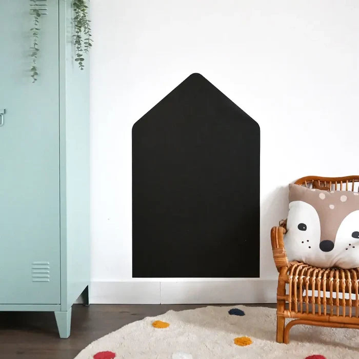 Large black house-shaped magnetic board on a white wall in a child's room next to a blue locker and wicker chair.