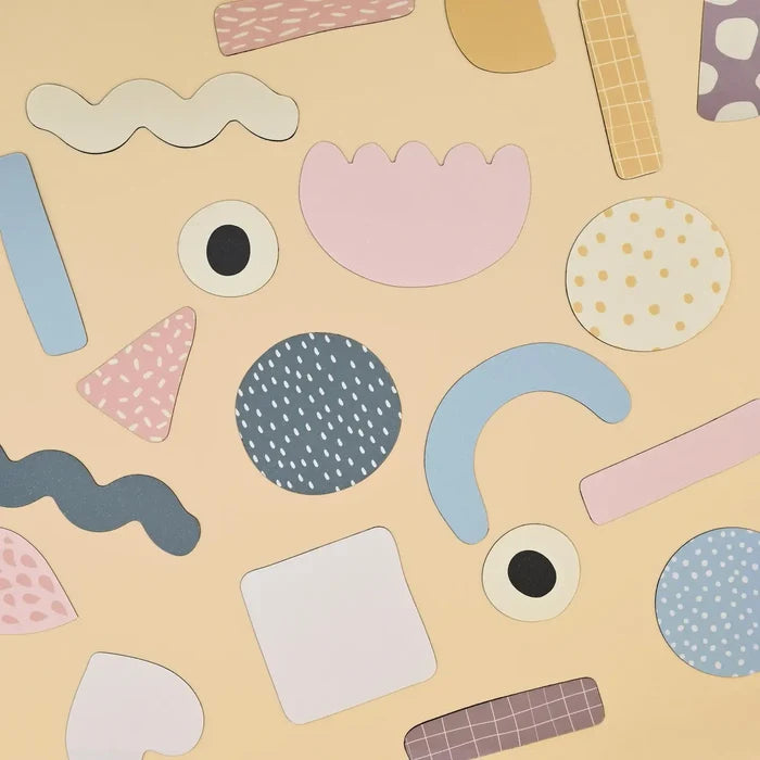 A collection of pastel-colored magnetic shapes in abstract and geometric patterns on a tan background.