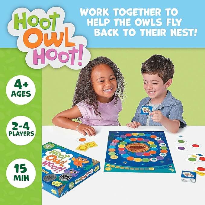 Two children smile while playing a board game with a colorful spiral path, round cards, and owl-themed box.