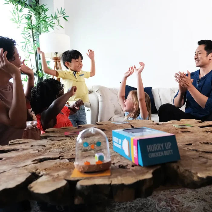 Diverse group cheers around a wood table with a blue Hurry Up Chicken Butt box and a clear dome dice shaker.