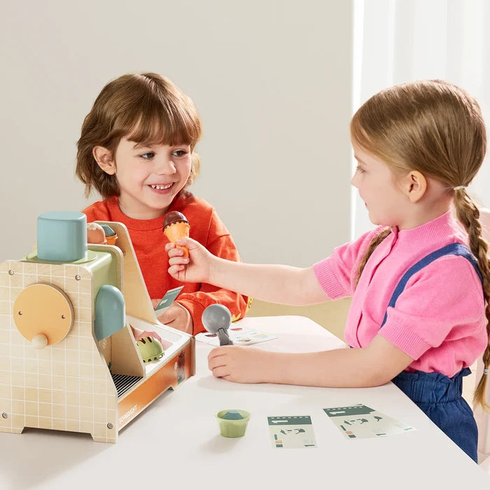 Two children play with a pastel-colored wooden toy stand, using a scoop and toy money to serve an ice cream cone.