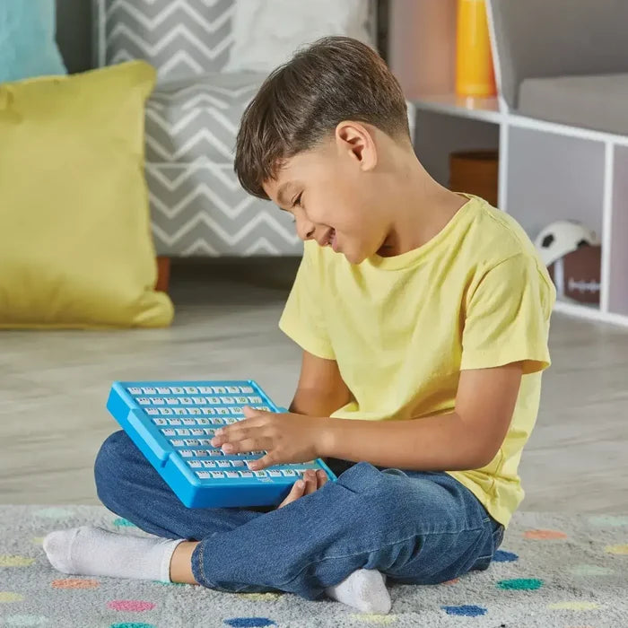 Young boy sitting on a rug playing with a blue addition board featuring rows of white pop-up number buttons.