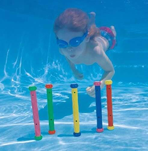 Child swimming underwater toward five colorful, upright cylindrical dive sticks standing on a pool floor.
