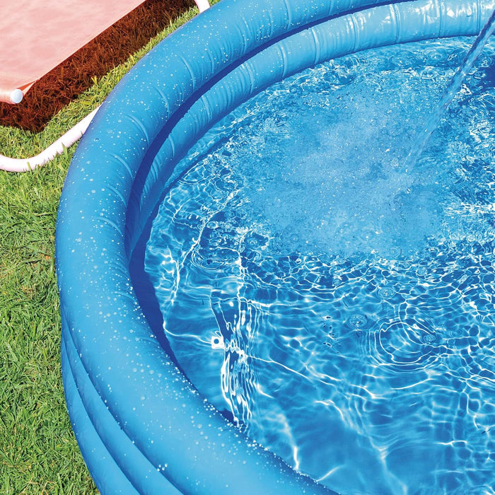 Close-up of a blue three-ring inflatable pool being filled with splashing water on a green lawn.