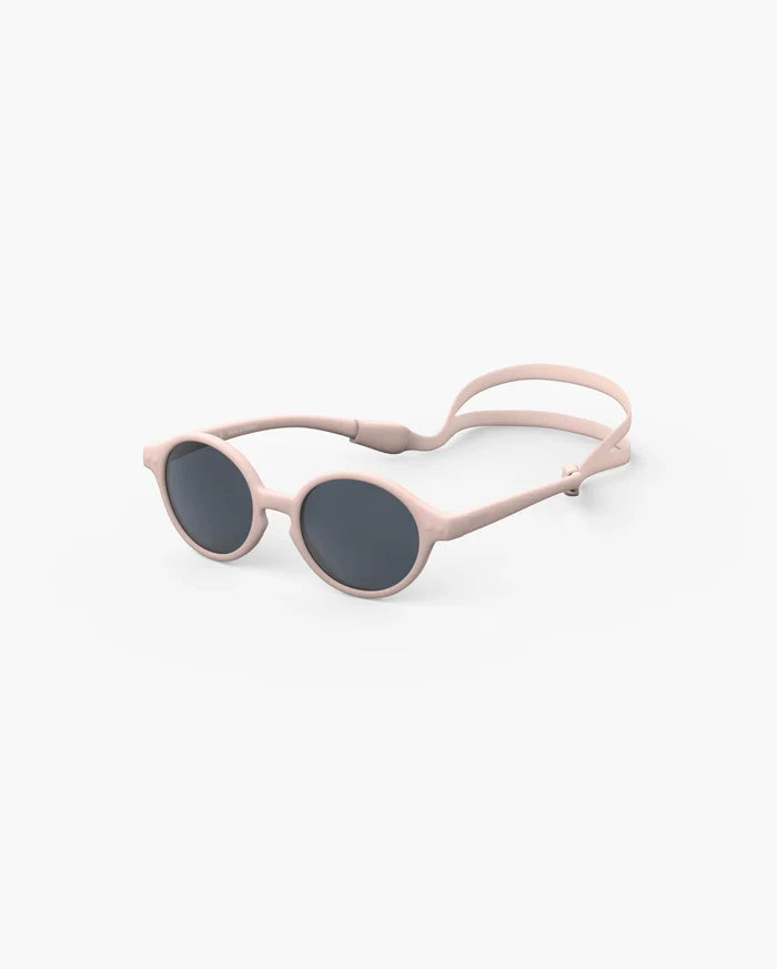Round, light pink sunglasses for infants with dark lenses and a matching silicone head strap on a white background.