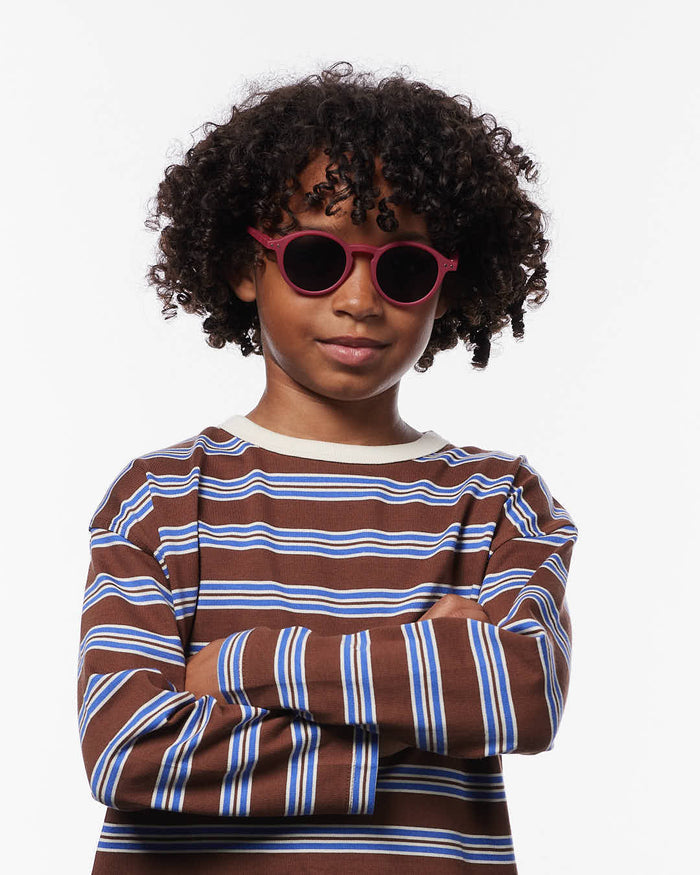 Child with curly hair wearing round magenta sunglasses and a striped brown shirt.