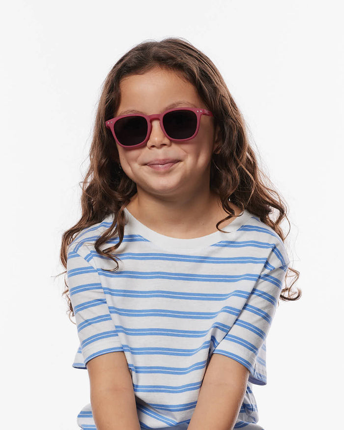 Young girl with long curly hair wearing burgundy square sunglasses and a blue and white striped t-shirt.