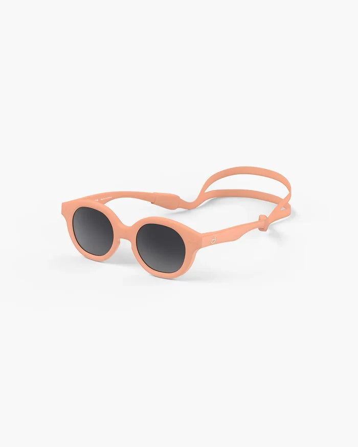 Round peach-colored baby sunglasses with dark lenses and an adjustable matching elastic head strap.
