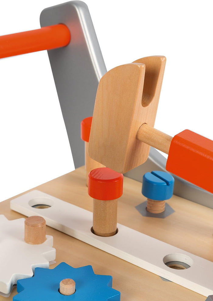 Close-up of a wooden toy hammer over a red peg, with a blue screw and colorful gears on a light wood play workbench.
