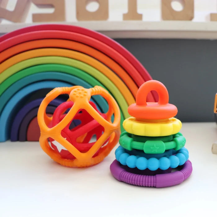 Textured five-ring silicone stacker in rainbow colors next to an orange geometric silicone teether ball.