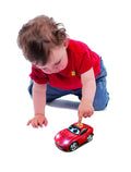 Toddler pressing a yellow button on a red Ferrari toy car with cartoon eyes and glowing headlights.