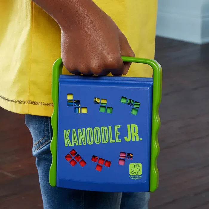 A child’s hand holding a blue case with a green handle and colorful puzzle pieces visible through shape cutouts.