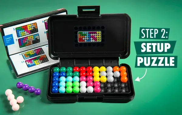 Open black case with colorful sphere puzzle pieces on a grid, loose pieces, and an instruction manual on a green surface.