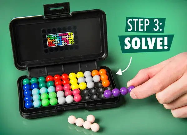 A person's hand places a purple beaded piece into a black portable game case filled with colorful 3D puzzle pieces.