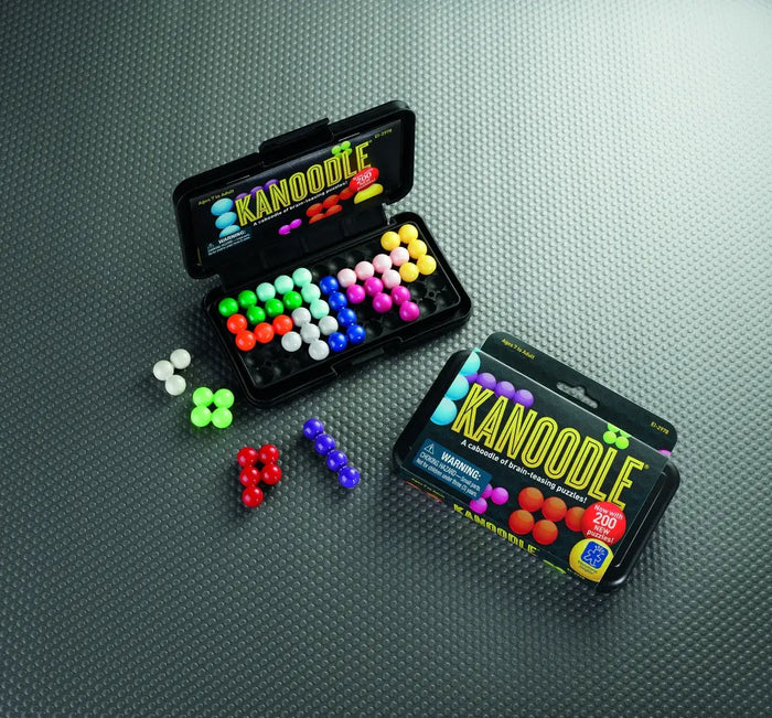 Open and closed black Kanoodle cases with colorful 3D bead puzzle pieces on a textured grey surface.