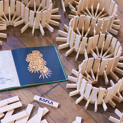 Green art book open to a building design next to complex circular structures made from light wood planks.