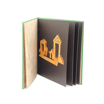 An open green art book with black pages showing a photograph of an intricate wooden plank archway structure.