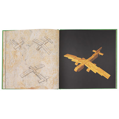 Open green-edged art book showing building steps and a photo of a wooden block airplane on a black background.