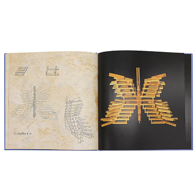 Open art book showing a golden wooden block butterfly sculpture and technical sketches on a parchment page.