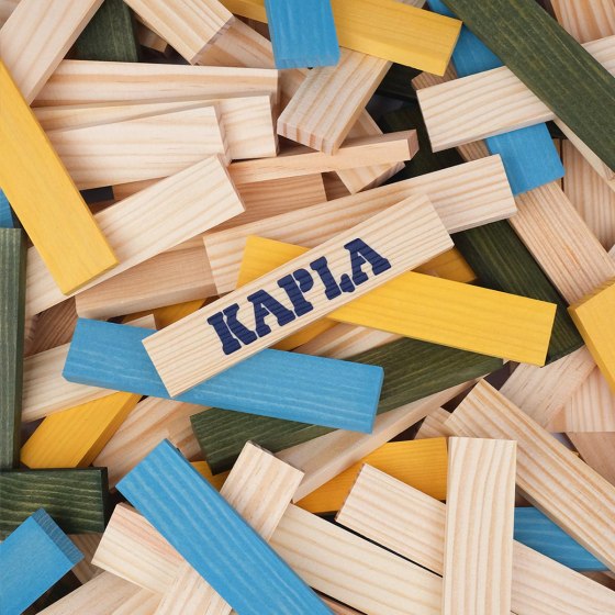 A pile of rectangular wooden blocks in light blue, yellow, green, and natural wood, with a Kapla logo on a center plank.
