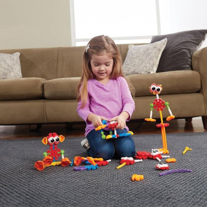 Young girl building colorful toy animals with bright plastic building pieces on a gray rug.