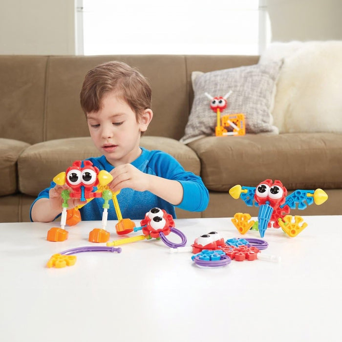 A boy building colorful plastic toy animals with big googly eyes and bright building pieces on a white table.
