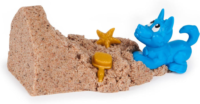 Blue toy dog sits in tan kinetic sand shaped like a dog house with gold starfish and brush accessories.