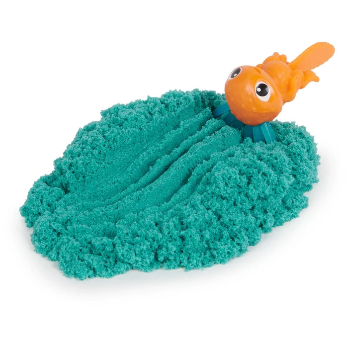 An orange toy creature making wavy tracks in a mound of textured teal kinetic sand.