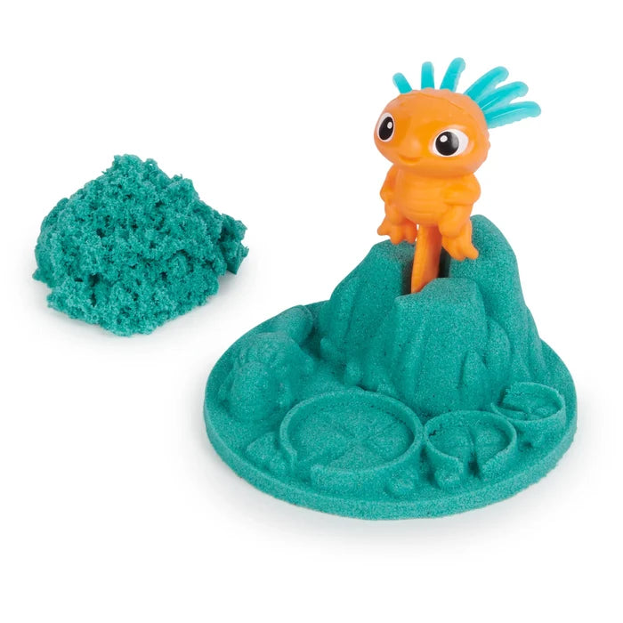 Orange toy with blue hair on a teal kinetic sand mountain base next to a separate pile of teal sand.