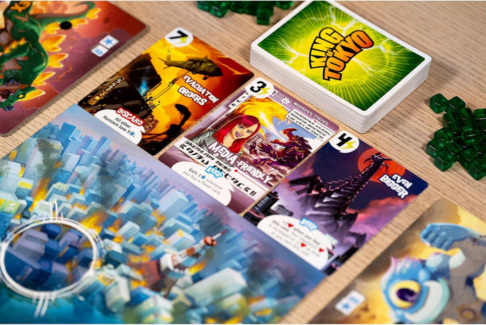 King of Tokyo cards, green energy cubes, and colorful monster boards spread out on a light wood table.