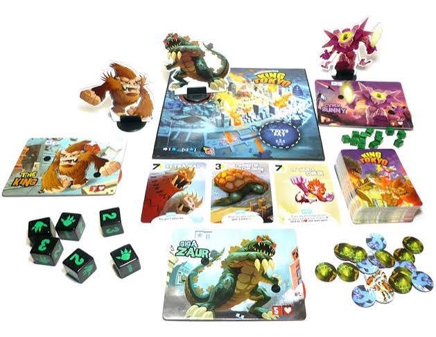A board game set laid out on a white background, including a central game board, multiple character figures, cards, dice, tokens, and boxes. The artwork shows colorful fantasy creatures and the title text 'The Dino Rush'.