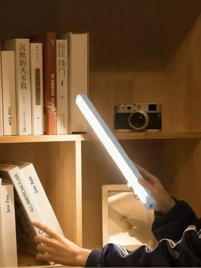 Person holding Kitchen Rechargeable Lamp LED Light With Motion Sensor illuminating books on a wooden shelf.