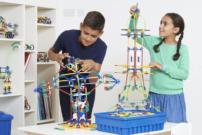 Two children building a tall tower and wheel with colorful plastic rods and connectors on a white table.