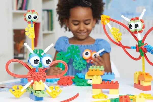 Child building colorful creatures with large eyes using green, blue, and red K'NEX connectors and flexible rods.